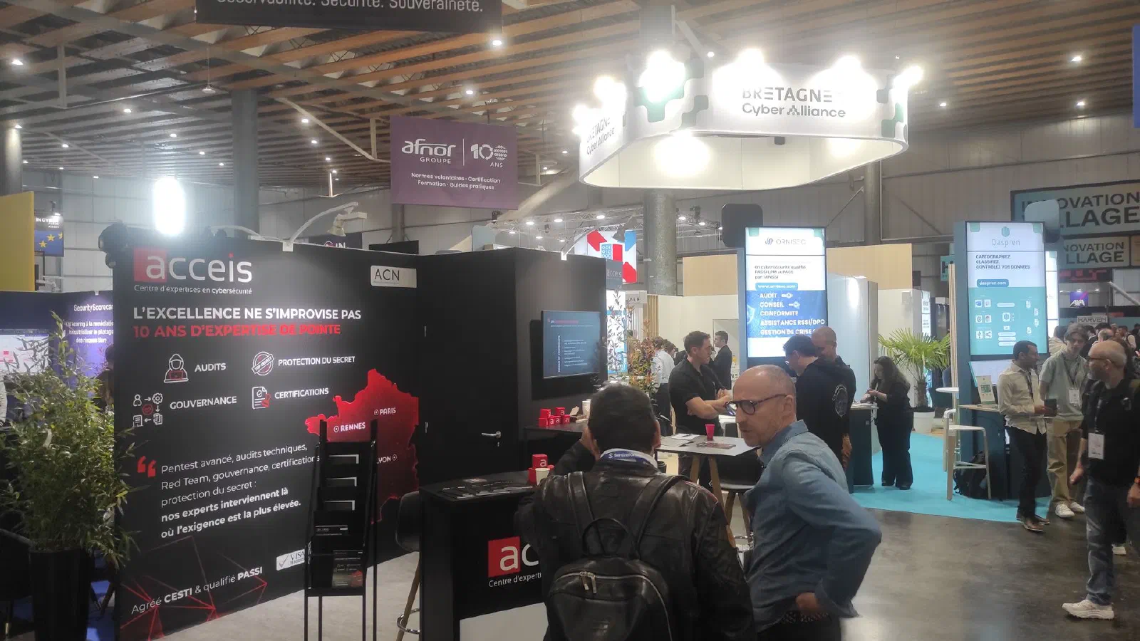 Stand ACCEIS au Forum InCyber à Lille Grand Palais : panneaux noirs et rouges présentant audits, gouvernance, protection du secret et certifications, carte de France situant Rennes, Paris et Lyon, visiteurs dans l'allée